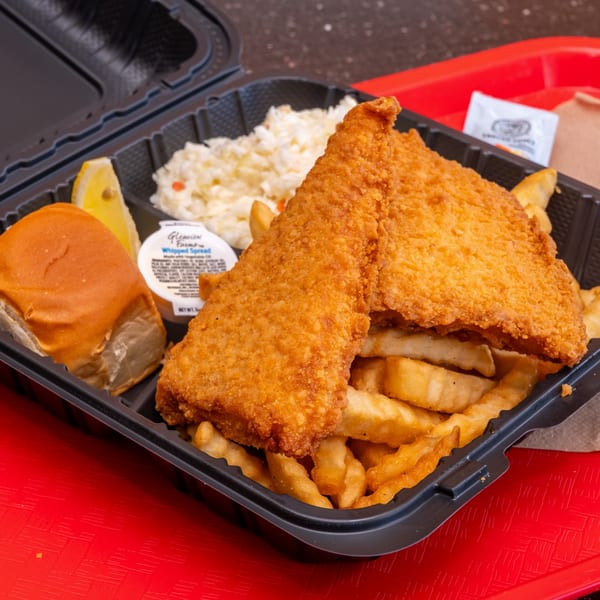 A Chili Hots fish and chips meal with coleslaw, a roll, and lemon wedge in a black takeout container.