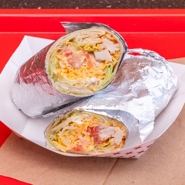 Two chicken wraps, filled with lettuce, cheese, and tomatoes, in foil on a red tray.