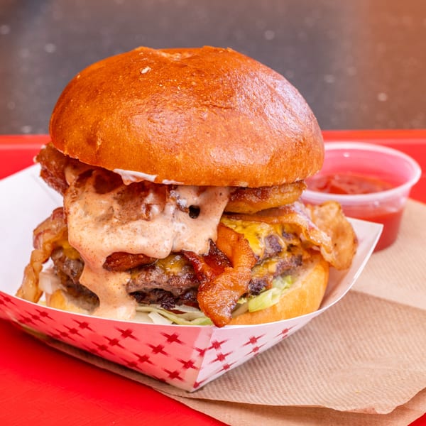 A Chili Hots double cheeseburger with bacon, onion rings, and special sauce, served with ketchup.