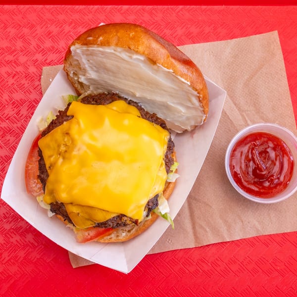 A Chili Hots cheeseburger with lettuce, tomato, and a side of ketchup on a red tray.