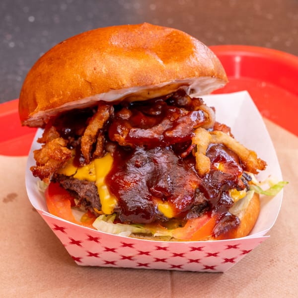 Chili Hots' BBQ burger with crispy onions, melted cheese, lettuce, and tomato in a paper tray.