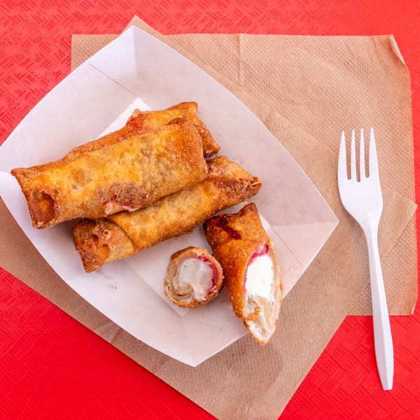 Fried dessert egg rolls with creamy filling, one cut open, in a paper tray with a white fork.