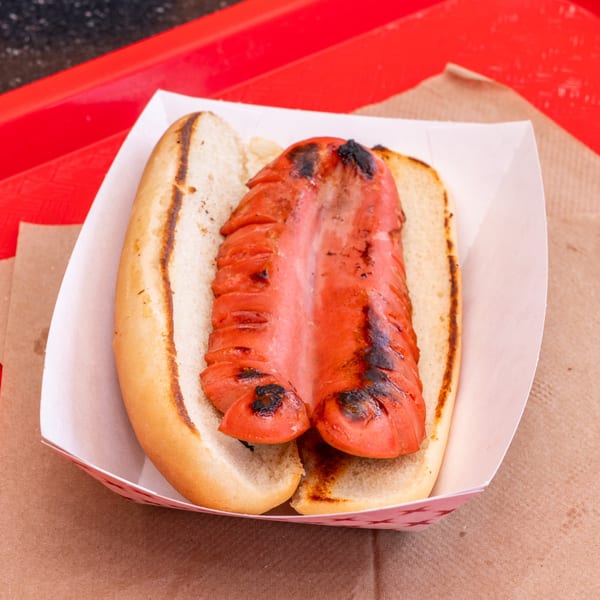 A grilled hot dog, split and charred, in a toasted bun, served in a paper tray.